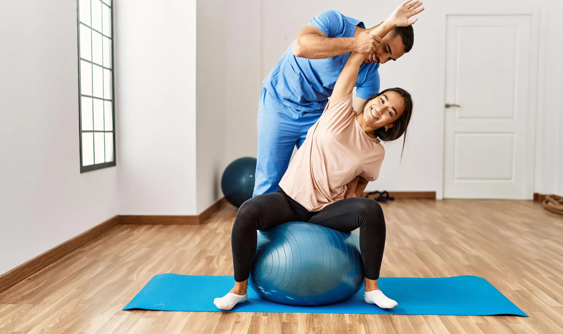 Bewegungstherapie im Reha-Zentrum Laab im Walde &ndash; Physiotherapeut unterst&uuml;tzt Patientin bei Dehn&uuml;bung auf Gymnastikball